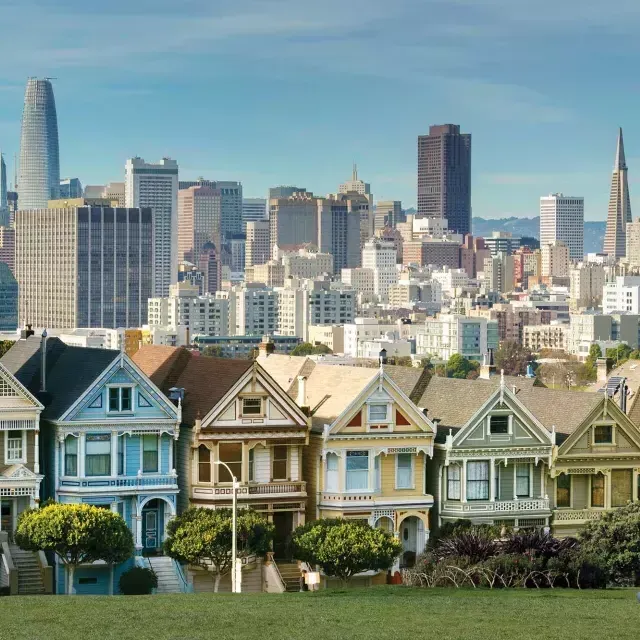 I picnic si siedono sull'erba ad Alamo Square Park con le Painted Ladies e lo skyline di San Francisco sullo sfondo.